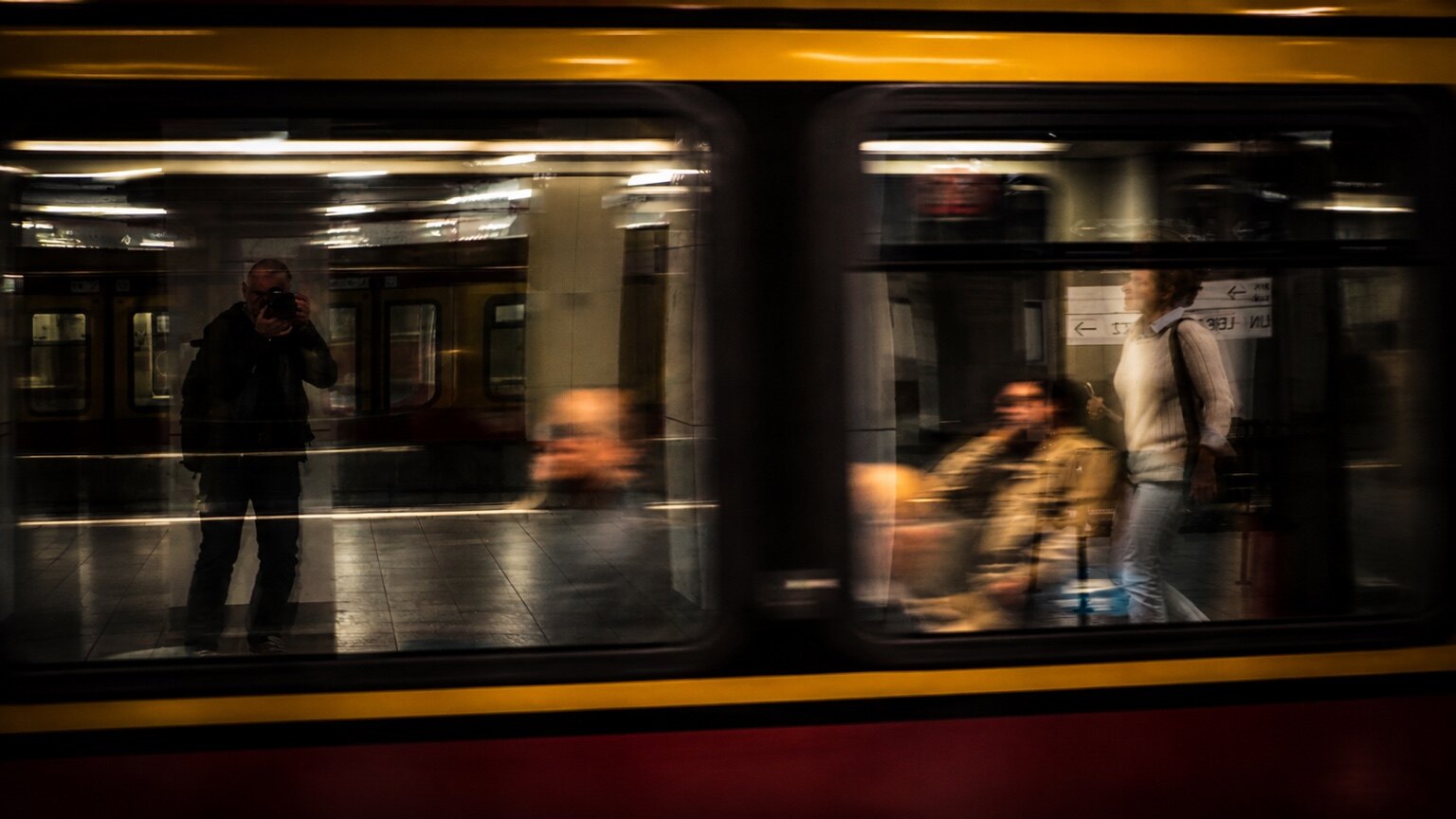Ein vorbeifahrender Zug; links spiegelt sich der Fotograf in der Scheibe.